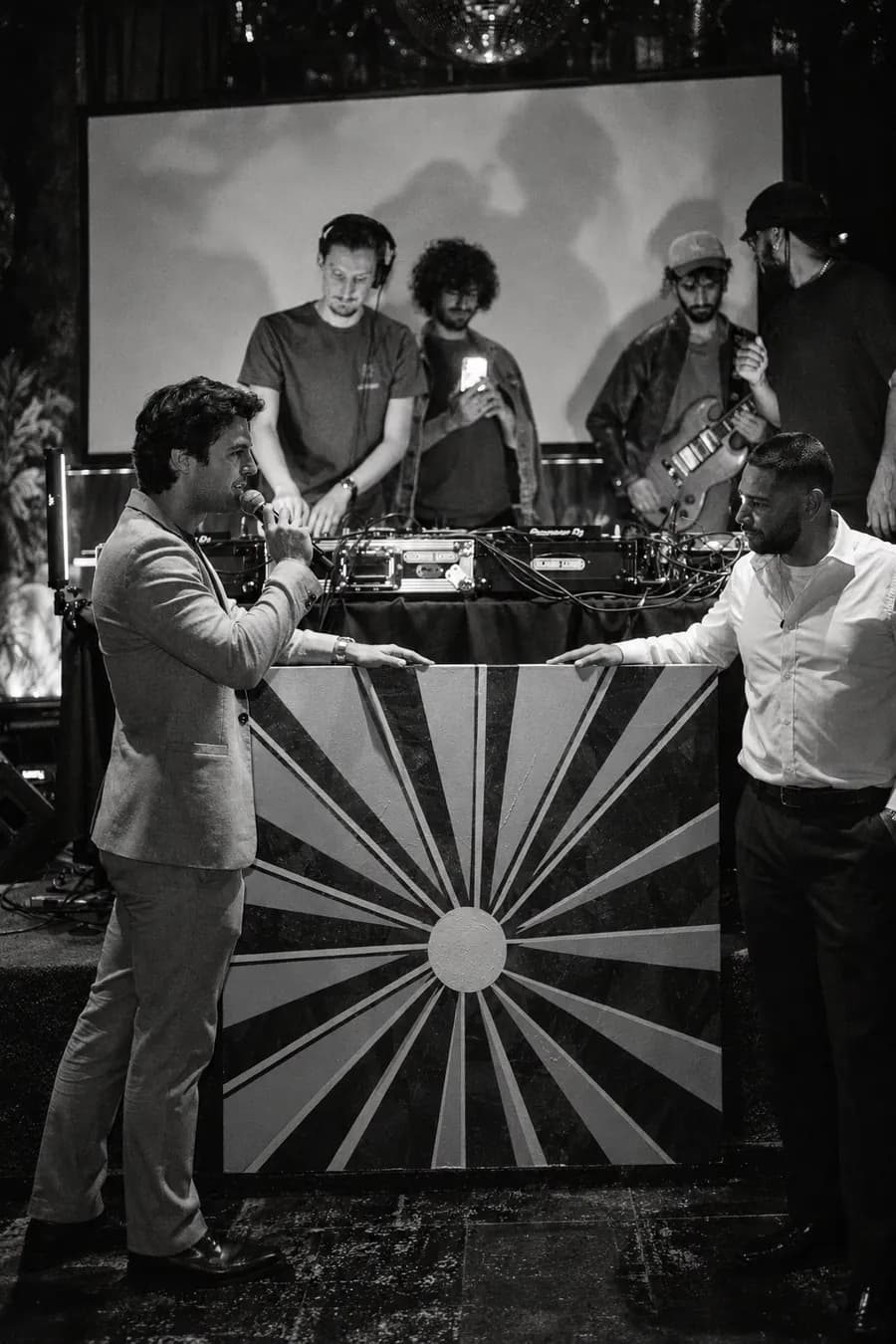Artists at the decks in a booth with a sunburst front, in black and white