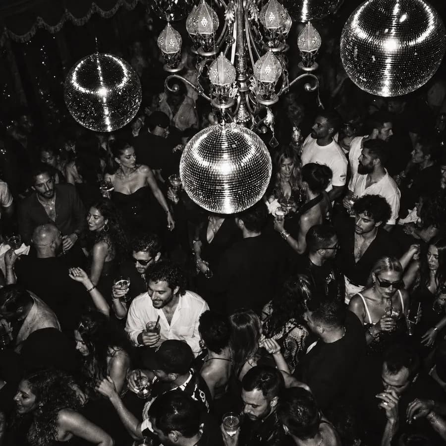 A packed room dancing under disco balls, in black and white